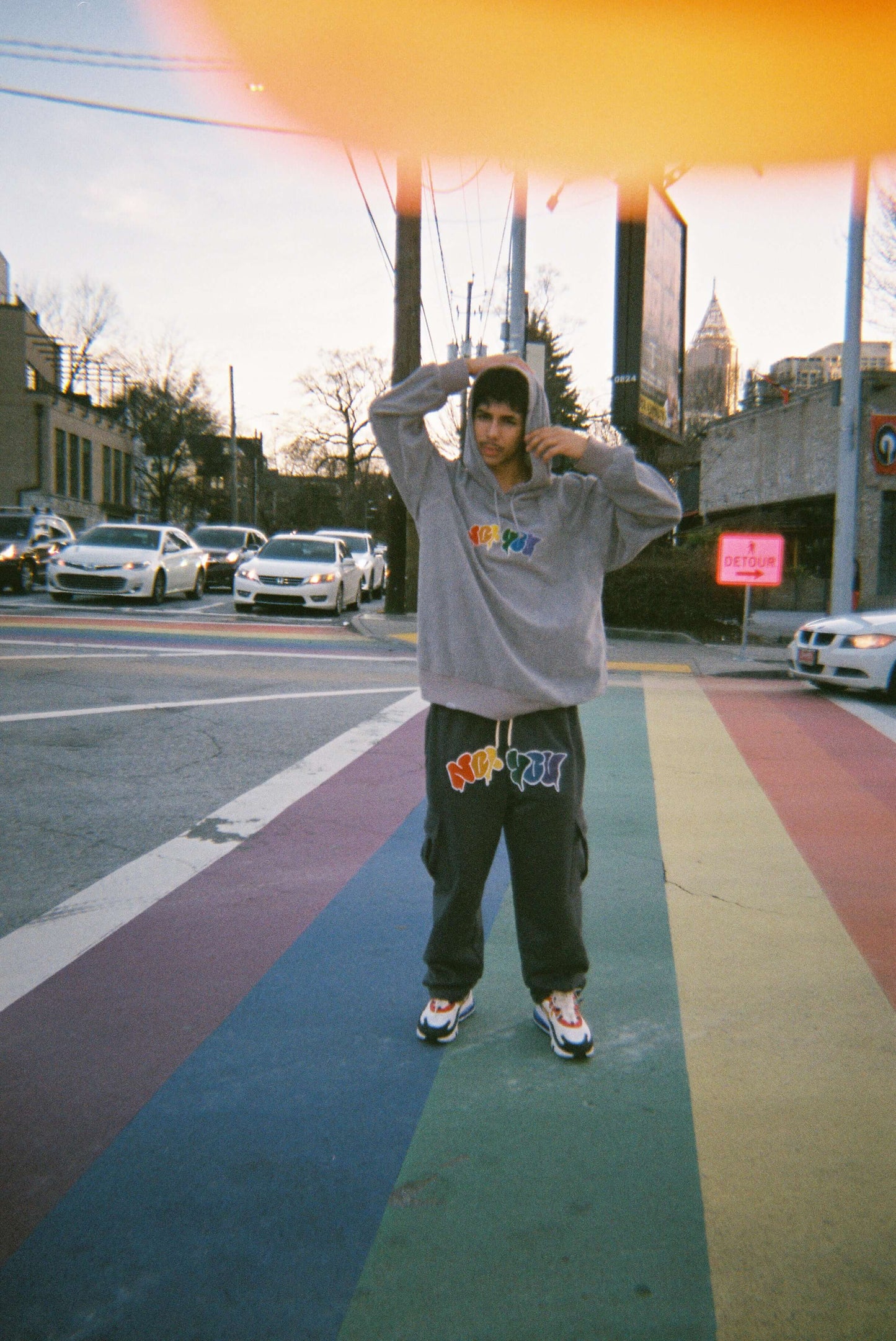 Model wearing Vibrance Cargo Pants Sweatpants and Hoodie on rainbow road